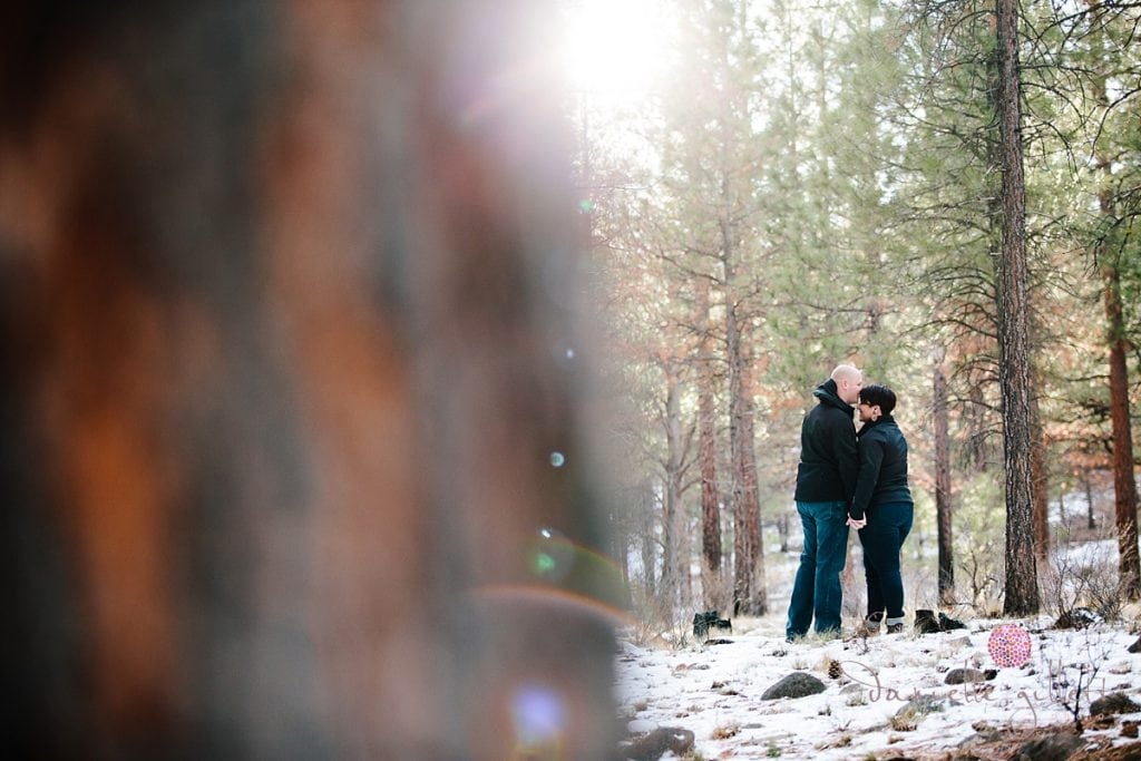 Sunkissed couple sneaking a kiss behind a tree in Bend Oregon engagement photos